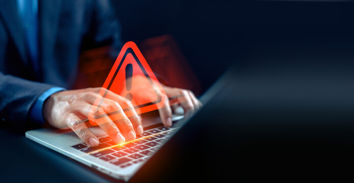 Businessman typing on laptop with glowing red warning exclamation sign hologram. Concept of cybersecurity risk, system error, online threat, and data breach security alert.