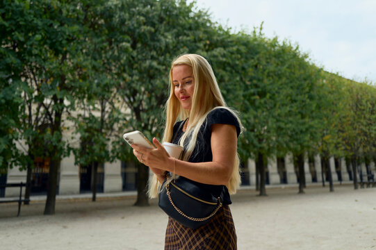 Woman with coffee scrolling on her phone in a city park