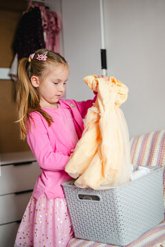 Young girl putting a yellow dress into a basket, tidying up her room