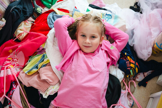 Young girl happily lies in a big pile of messy clothes