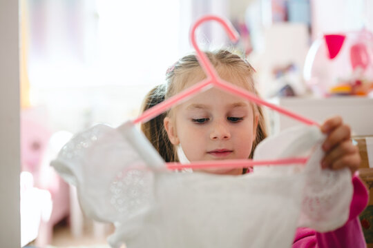 Young girl holding a hanger with a white dress deciding what to wear