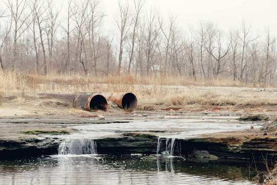 Rusty industrial pipes draining into a polluted stream