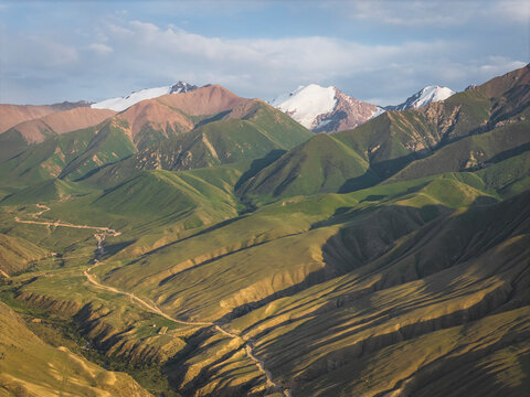 Winding road through green hills and snowy mountains