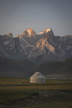Traditional yurt in a valley with snowy mountains at sunrise