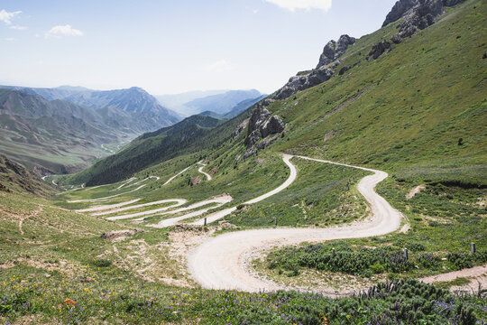 A winding dirt road snakes through a lush green mountain pass