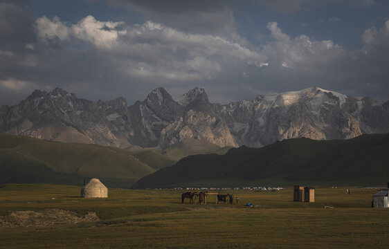 Yurt and horses in a valley below snow capped mountains