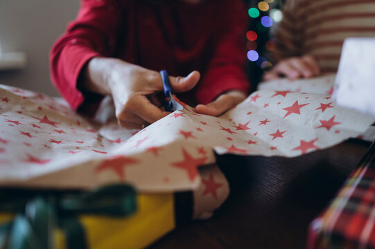 Woman cuts star wrapping paper for Christmas gifts at home with boy