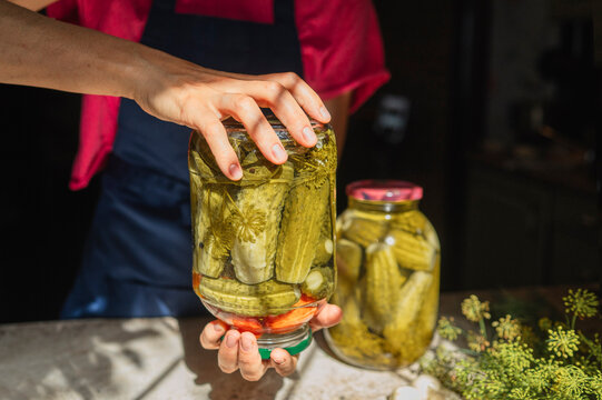 Woman holds a glass jar of pickled cucumbers in the kitchen