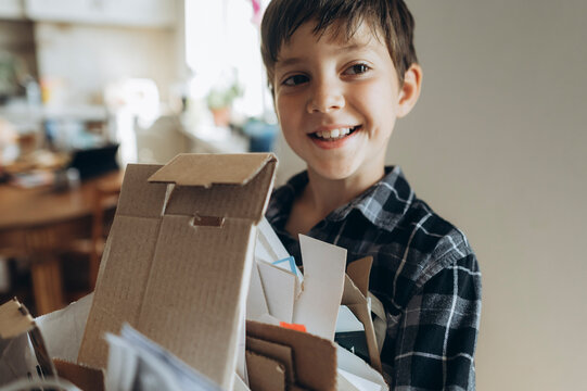 A smiling boy holds a box of cardboard for recycling at home