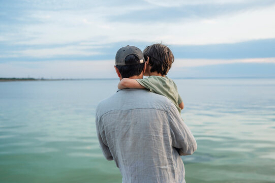 A father carries his son while looking at the sea on summer vacation