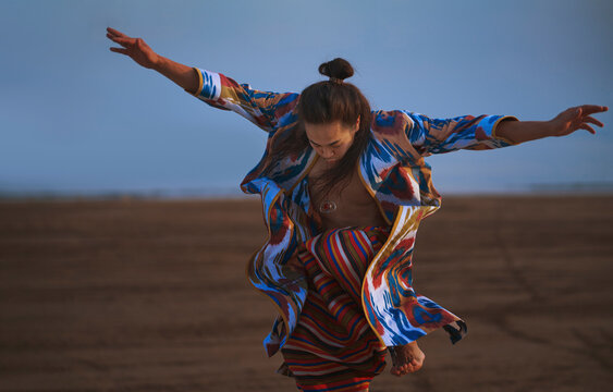 A man wears a colorful patchwork robe while dancing in the desert