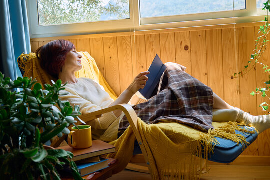 Woman reads a book while relaxing in an armchair by the window