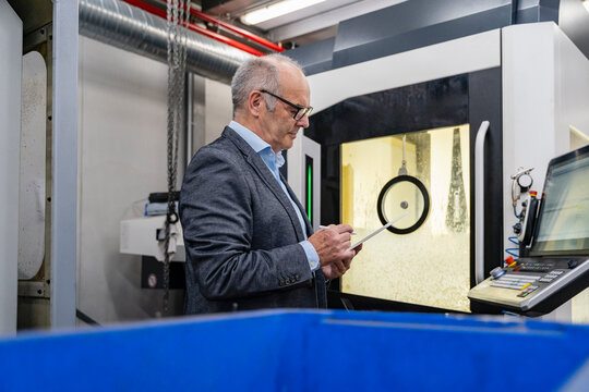 Male manager using tablet by machinery in production hall
