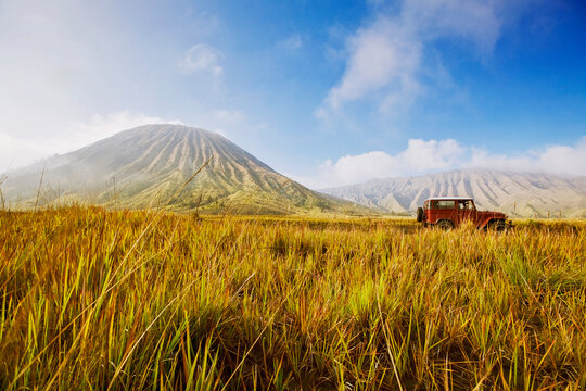 A red jeep stands in tall savanna grass near Mount Bromo in Indonesia