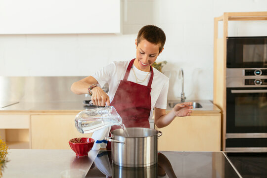 Woman boiling water in cooking pot in kitchen