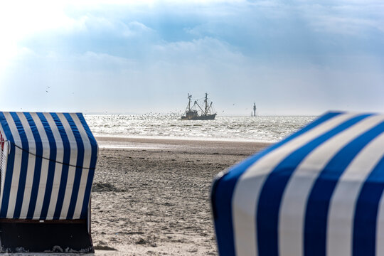 Fishing boat sails on the North Sea behind a striped beach chair