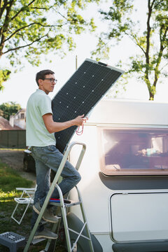 Man installs a solar panel on the roof of a camper at a campsite