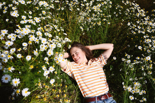 Smiling woman lying in a summer field of daisy flowers