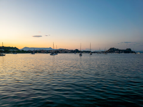 Beautiful Sunset Over Garitsa Bay with Sailboats and Old Fortress in Corfu Town, Greece
