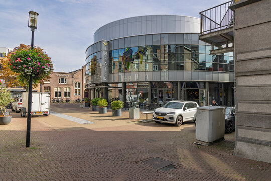 Purmerend, Netherlands - September 27, 2026: Exterior view of Theater De Purmaryn, featuring a modern curved glass facade, situated in a bustling urban square with parked cars.