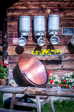 A copper cheese cauldron sits by a wooden wall with milk pails