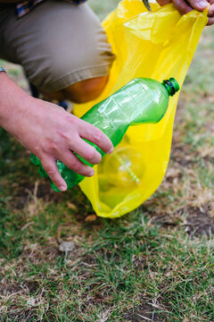 Man puts green plastic bottle into yellow garbage bag outdoors