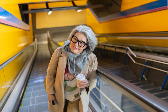 Stylish woman with coffee on metro escalator in city setting