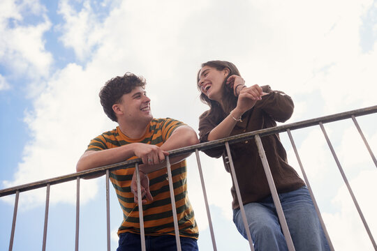 Happy man and woman laughing and leaning on railing outdoors