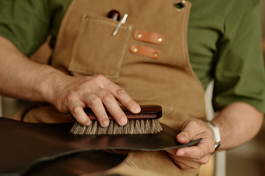 Male artisan prepares handmade leather with a brush in his workshop