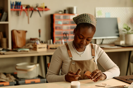 Woman artisan working with leather at workbench in her studio
