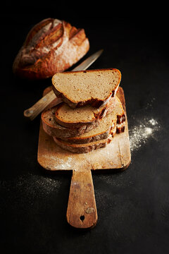 Sliced rustic bread stacked on a wooden cutting board with a knife