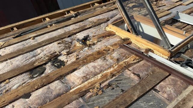 Exposed roof framing, deteriorated insulation, debris, and a removed skylight reveal extensive damage during residential roof repair work