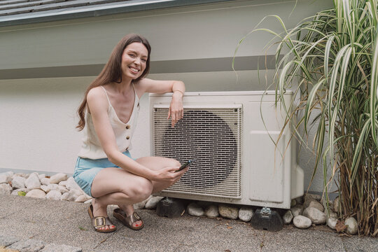 Woman controls home heat pump with smartphone app outdoors
