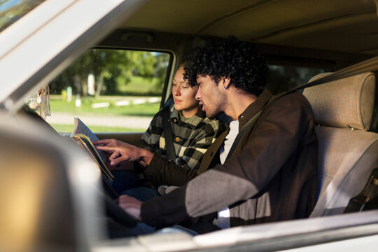 A young couple plans their road trip route on a map inside a van