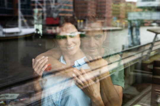 Smiling couple embracing indoors behind a window with city reflection