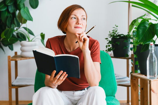 Thoughtful woman holds an open notebook in her home office