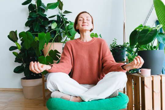 Peaceful woman practices meditation among lush indoor houseplants