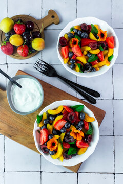 Fresh fruit salad and yogurt sit on a white tiled table indoors