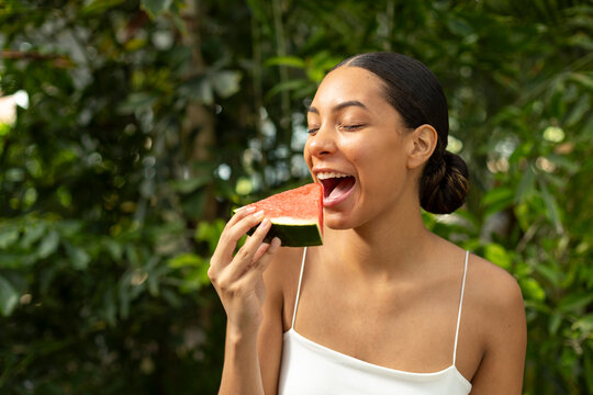 A happy woman eats a refreshing watermelon outdoors in summer