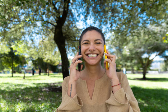 Smiling woman in a park holding two smartphones to her ears
