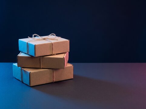 Three stacked cardboard boxes tied with twine, illuminated by blue and pink light on a dark background.