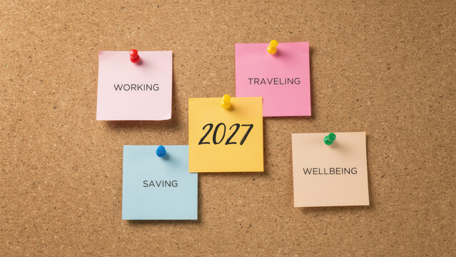 Sticky notes with life goals for the year 2027 pinned to a brown cork board with five colorful sticky notes text regarding goals attached push communication working