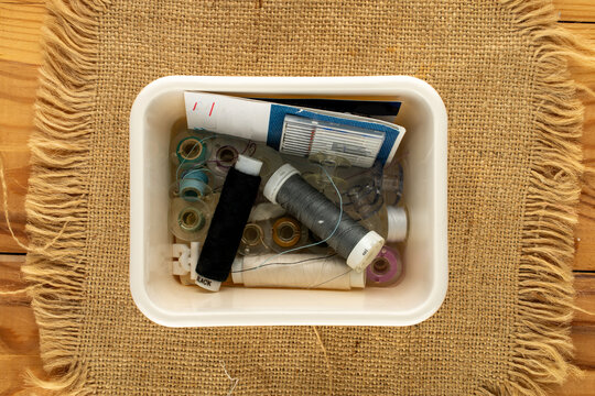 Small but essential sewing items in a plastic box on jute fabric; macro shot, top view.