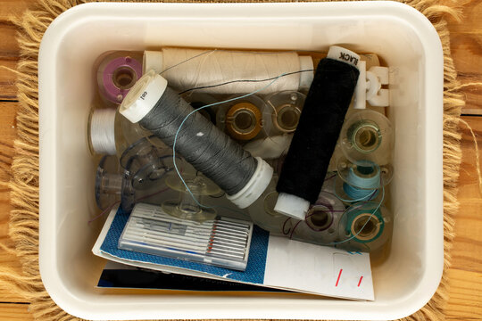 Small but essential sewing items in a plastic box on jute fabric; macro shot, top view.