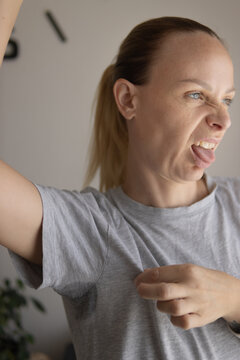 Woman experiencing body odor and hyperhidrosis, raising her arm to reveal a large sweat stain on her gray t-shirt, showing discomfort and hygiene issues