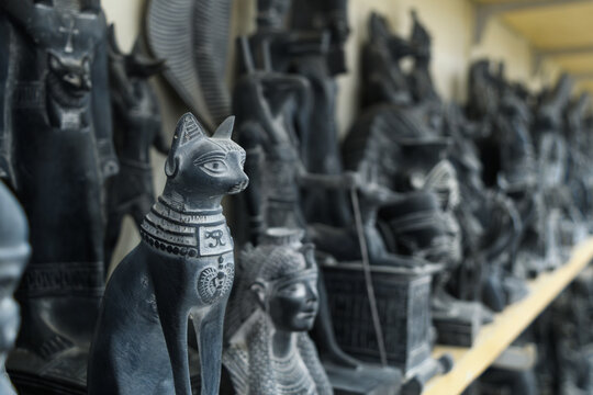 Black cat figurine stands among Egyptian souvenir statues on shop shelf in Egypt.