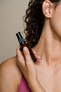Hispanic woman holding amber spray bottle near neck in beauty shoot