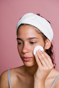 Hispanic woman applying skincare with a cotton pad and white headband