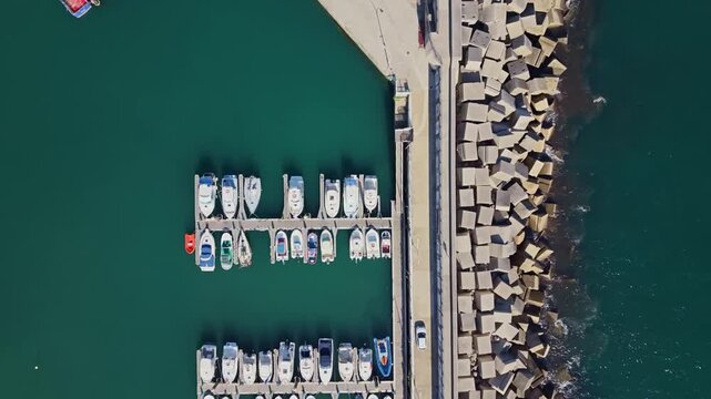 Aerial vertical view of port pier separating ocean breakwater and moored boats in marina dock Candas Spain