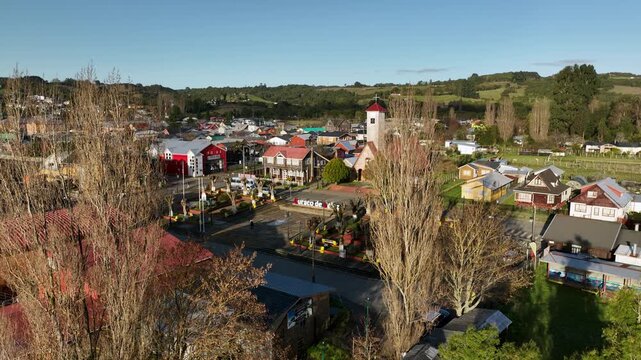 A slow aerial glide moves toward the heart of Curaco de V&eacute;lez, its white bell tower and colorful storefronts framed by bare autumn poplars beneath the calm Chilo&eacute; countryside.